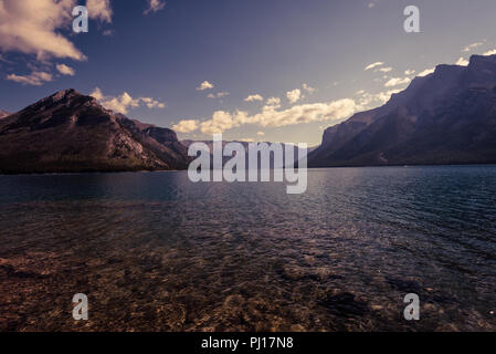 Schatten über Lake Minnewanka, umgeben von Bergen. Stockfoto