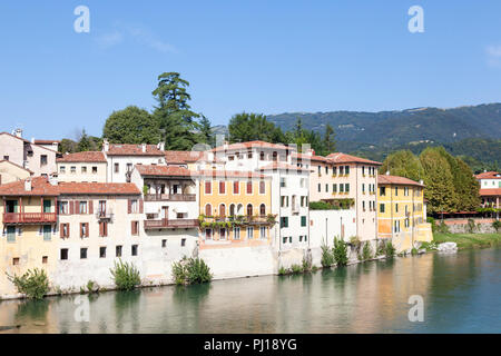 Bunte Häuser auf dem Brenta Fluss, Bassano del Grappa, Vicenza, Italien im frühen Morgenlicht mit Reflexionen und Blick auf die Dolomiten. Stockfoto