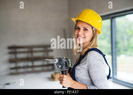 Junge Frau Arbeiter, der mit einem gelben Helm und elektrische Bohrmaschine auf der Baustelle. Stockfoto