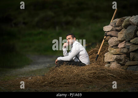 Landwirt sitzt auf einem Haufen Heu, Irland Stockfoto