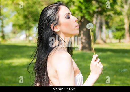 Schöne schwarze Haare Mädchen mit Löwenzahn in der Hand in der Natur Stockfoto