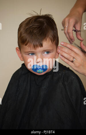 Junge (3 Jahre alt) mit Dummy im Mund und sich die Haare schneiden, England, UK. Stockfoto