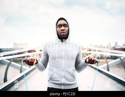 Junge aktive schwarze Sportler überspringt mit einem Seil in einer Stadt, hoodie tragen. Stockfoto