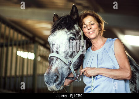 Eine ältere Frau, die in der Nähe eines Pferdes in eine stabile, es halten. Stockfoto