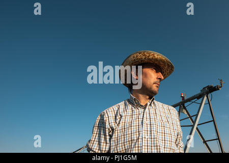 Ernsthafte betroffenen Landwirt in Maisfeld mit Bewässerungsanlage außer Betrieb während der warmen Sommertag Stockfoto