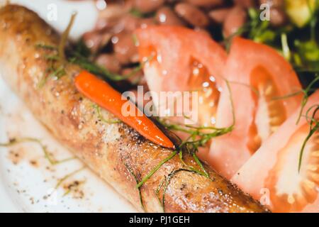 Auf einem weißen Teller mit einer Portion Option liegt eine köstliche Mahlzeit. Gewürze sind bestreut mit frischen Gurken, rote Bohnen, Tomaten, Dill und Fried in einem Skil Stockfoto