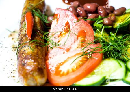 Auf einem weißen Teller mit einer Portion Option liegt eine köstliche Mahlzeit. Gewürze sind bestreut mit frischen Gurken, rote Bohnen, Tomaten, Dill und Fried in einem Skil Stockfoto