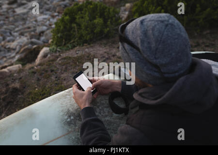 Mann mit Surfbrett mit mobilen am Strand Stockfoto