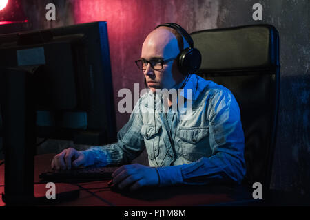 Ernster junger Mann sitzen und arbeiten mit Computer im dunklen Büro Stockfoto