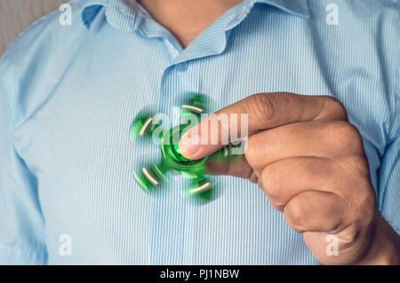 Ein Mann hand Halten einer Hand grüne Spinner oder zappeln Spinner auf dem Hintergrund. Leistungsstarke Spinner, Twister für Hände Unterhaltung rotierende Spielzeug. Antistres Stockfoto