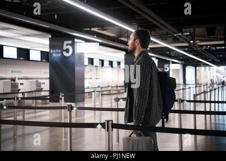 Junger Mann mit seinem Gepäck und Sie Ihr Smartphone während des Wartens auf Airline Flight im international airport terminal Rucksack, Reisen und online Check-in-Konzepte Stockfoto