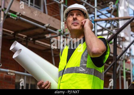 Männliche builder Vorarbeiter, Arbeiter oder Architekt auf der Baustelle holding Baupläne und über sein Mobiltelefon Stockfoto