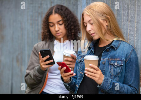 Interracial Freunde hübsche Blondine Jugendlicher und Mixed Race African American Girl weibliche junge Frau mit Ihrem smart phones für Social Media und Trinken Stockfoto