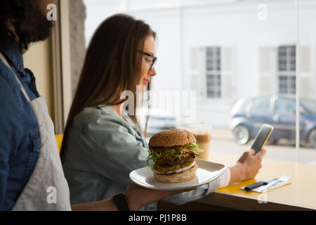 Kellner Burger, Frau, während mit Handy Stockfoto