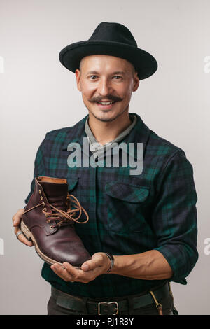 Foto der jungen fröhlichen Schuster Holding selbst gemacht Schuh über Weiß isoliert. Stockfoto