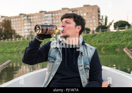 Bärtiger Mann sitzt auf einem Boot rum Trinken aus der Flasche Stockfoto