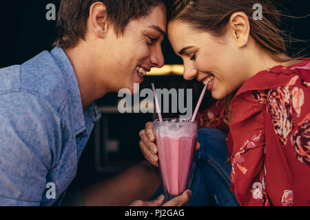 Nahaufnahme von einem glücklichen Paar in einem Milchshake mit zwei strohhalme. Lächelnd Mann und Frau auf einem Datum sitzen in einem Restaurant in einem Milchshake. Stockfoto