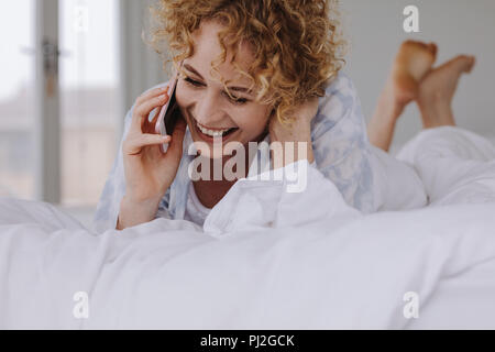 Frau Gespräch am Handy, während sie sich auf dem Bett. Frau Gespräch am Handy im Bett lag. Stockfoto