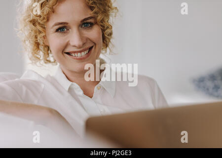 Porträt eines lächelnden Geschäftsfrau, die an einem Notebook arbeitet. Braune lockige behaarte Frau zu Hause sitzen Arbeiten am Laptop. Stockfoto