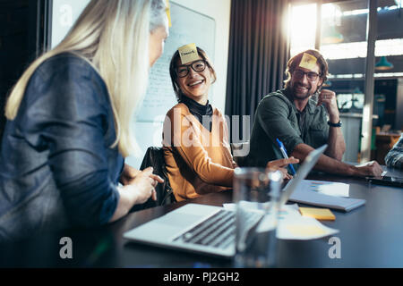 Lächelnd asiatische Frau mit Zettel auf der Stirn sitzt mit Kollegen treffen. Diverse Business Team ein Brainstorming in Board Stockfoto