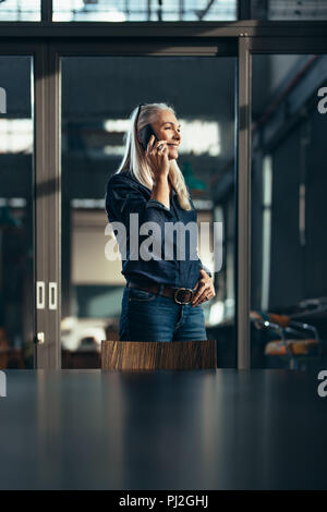 Lächelnd reife Geschäftsfrau in casuals Gespräch am Handy. Leitende Führungskraft im Büro anrufen. Stockfoto