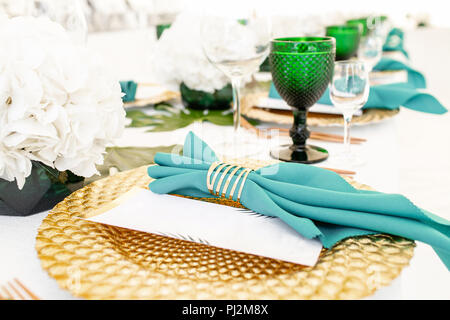 Innenraum des Zeltes für Hochzeit Diner, bereit für die Gäste. Runde Tafel im Freien serviert im Festzelt dekoriert Hortensienblüten, goldene Teller und Servietten. Catering Konzept Stockfoto