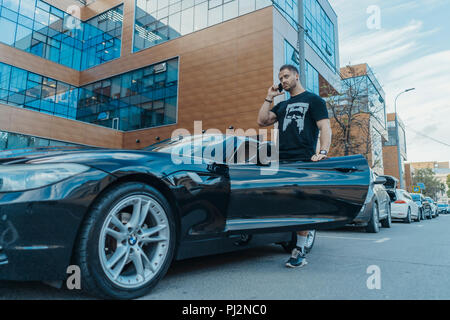 Junger Mann aus dem schwarzen Auto und sprechen per Handy. Von der Seite. Stockfoto