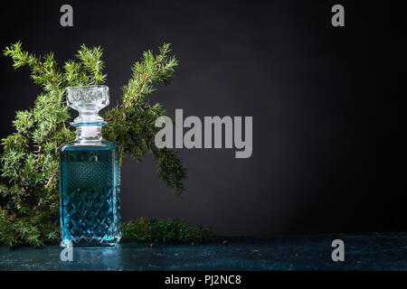 Blue Gin in Kristall Karaffe und Juniper Zweig mit Beeren auf einem schwarzen Hintergrund. Kopieren Sie Platz für Ihren Text. Stockfoto