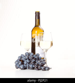 Zwei Gläser und eine Flasche Weißwein, auf einem weißen Hintergrund in der Nähe von einer Handvoll Trauben Stockfoto