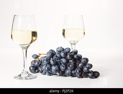 Zwei Gläser und eine Flasche Weißwein, auf einem weißen Hintergrund in der Nähe von einer Handvoll Trauben Stockfoto