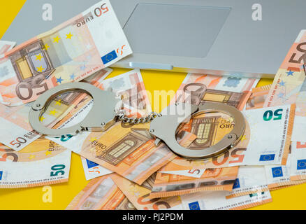Handschellen mit Geld auf der Tastatur des Laptops. Stockfoto