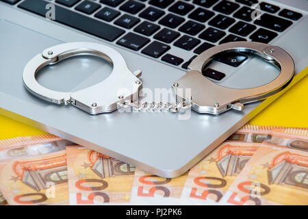 Geld unter Handschellen auf der Tastatur des Laptops. Hacker Kriminalität Konzept. Stockfoto
