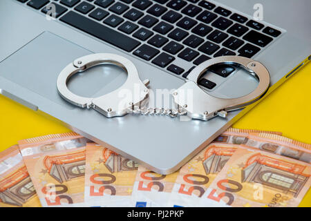 Geld unter Handschellen auf der Tastatur des Laptops. Hacker Kriminalität Konzept. Stockfoto