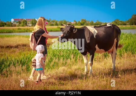 Junge Mutter mit Kindern streicheln grosse Kuh auf der Straße Stockfoto