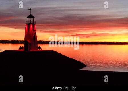 Der Leuchtturm am See Hefner Ostkaje in Oklahoma City Leuchtet rot gegen eine bunte bewölkt, Sonnenuntergang, mit Menschen auf Bänken. Stockfoto