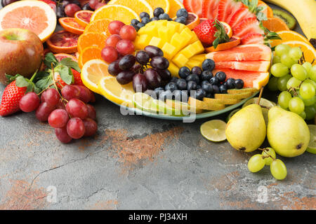 Gesunde Früchte Hintergrund in Regenbogenfarben Orangen, Äpfel, Trauben, Birnen, Mango, Erdbeeren, Kiwis auf dem grauen Beton Tabelle, Kopieren, selektiven Fokus Stockfoto