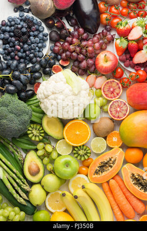 Das gesunde Essen Hintergrund, eine Auswahl an verschiedenen Früchten und Gemüse in Regenbogenfarben an der aus weissen Tisch in einem Rechteck, Ansicht von oben angeordnet, selektiver Fokus Stockfoto