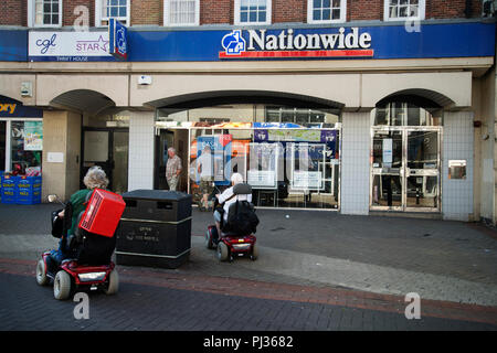 Hastings, East Sussex. Zwei ältere Menschen auf Mobilität scooters pass Nationwide Building Society Stockfoto