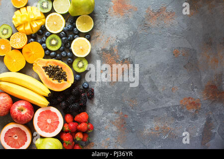 Blick von oben auf die regenbogenfarbenen Früchte und Beeren auf den grauen Stein, kopieren Platz für Text, selektiver Fokus Stockfoto