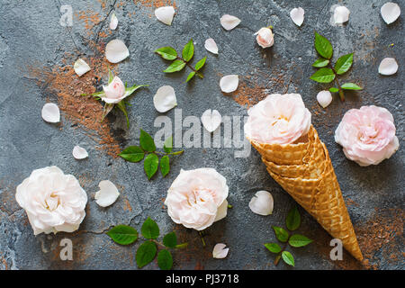 Eistüten mit Rosen, Overhead Zusammensetzung mit Blumen, Blüten, Blätter auf dem grauen Beton Hintergrund Stockfoto