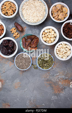 Vielzahl von inngredients für hausgemachtes Müsli, Hafer, verschiedene Nüsse und Rosinen, Datteln, Samen auf dem grauen Stein Hintergrund, Ansicht von oben Stockfoto