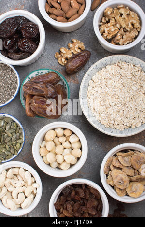 Zutaten für hausgemachtes Müsli, Hafer, verschiedene Nüsse und Rosinen, Datteln, Samen auf dem grauen Stein Hintergrund, Ansicht von oben Stockfoto