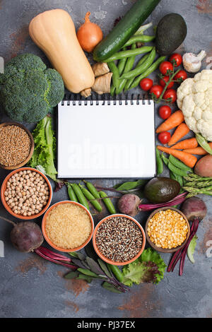 Buntes Gemüse und Getreide, in einem Kreis mit einem weißen Notebook in der Mitte, Brokkoli, Kürbis, Bohnen, Tomaten, Möhren, Avocado angeordnet, Ansicht von oben Stockfoto