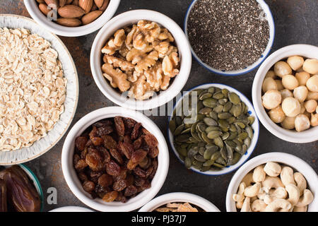 Zutaten für hausgemachtes Müsli, Hafer, verschiedene Nüsse und Rosinen, Datteln, Samen auf dem grauen Stein Hintergrund, Ansicht von oben Stockfoto