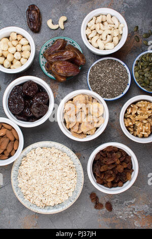 Oben Ansicht von Zutaten für hausgemachtes Müsli, Hafer, verschiedene Nüsse und Rosinen, Datteln, Samen auf dem grauen Stein Hintergrund, selektiver Fokus Stockfoto