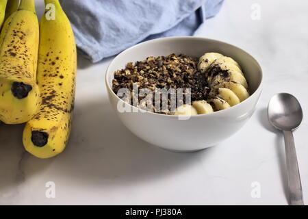 Schüssel mit hausgemachtem Müsli mit Bananen-, Kakao- und Johannisbrot Stockfoto