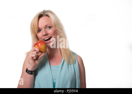 Blonde Frau mit einem Lächeln mit einem Apfel Stockfoto