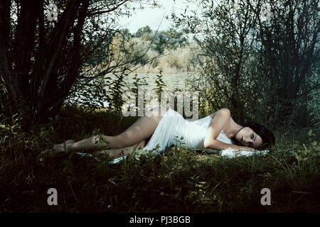 Blassen Frau in weißem Kleid auf dem Boden liegend, märchenhafte Szene Stockfoto