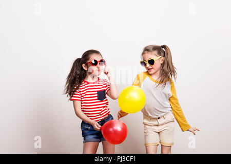 Kleine Mädchen mit Sonnenbrille und Luftballons in einem Studio. Stockfoto