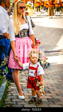 Frau und Sohn beobachten die Prozession von Männern und Frauen in traditionellen Kostümen auf dem Dorfplatz vom Mäzenatentum Tag in Reith bei Seefeld, Österreich Stockfoto